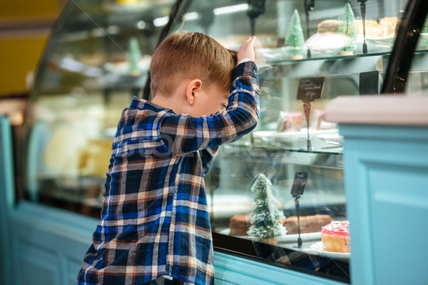 Little boy standing and leaning at shocase with cakes Stock photo © deandrobot