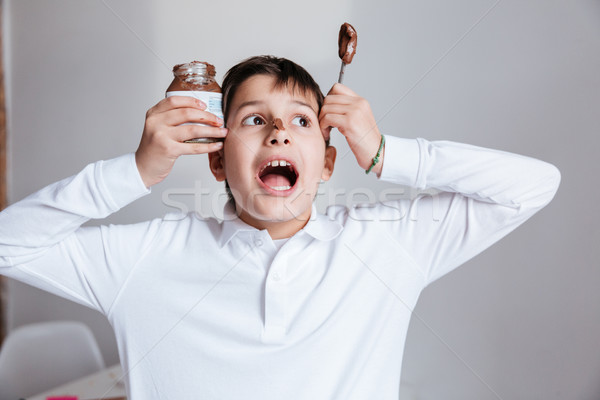 Amusing little boy eating chocolate spread from jar and shouting Stock photo © deandrobot