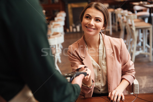 Attractive young pretty woman sitting in cafe pays the order Stock photo © deandrobot