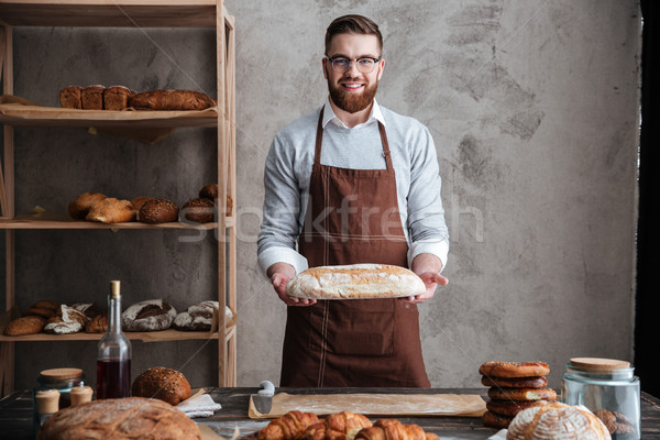 Cheerful young man baker standing at bakery holding bread Stock photo © deandrobot