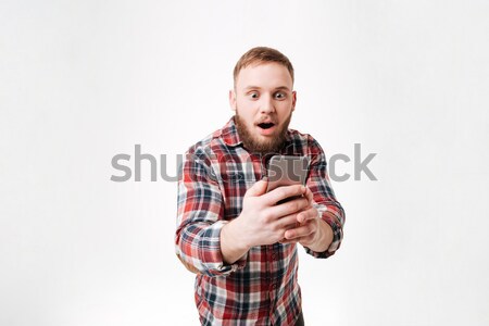 Happy bearded man in checkered shirt playing on his smartphone Stock photo © deandrobot