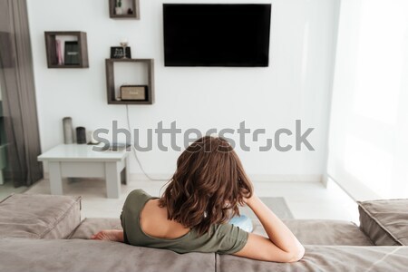 Back view of woman sitting on sofa and watching TV Stock photo © deandrobot