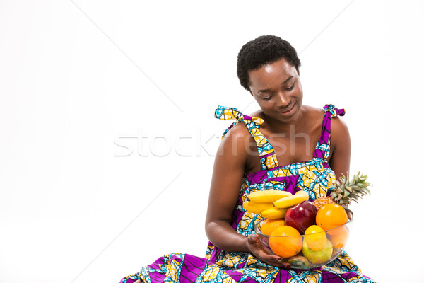 Stock photo: Pretty happy african woman sitting and looking at fresh fruits 