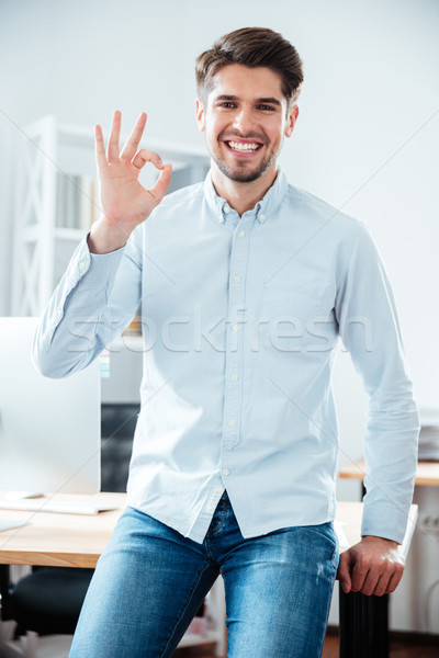 Smiling young businessman standing and showing ok sign Stock photo © deandrobot