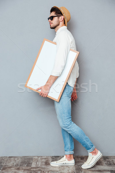 Attractive young man walking and holding blank white board Stock photo © deandrobot