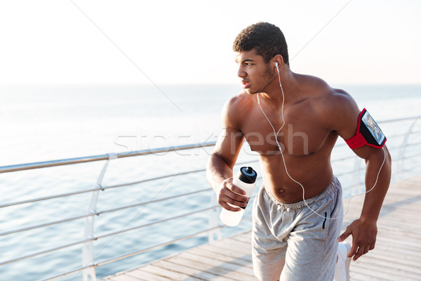 Serious african sportsman running and listening to music outdoors Stock photo © deandrobot