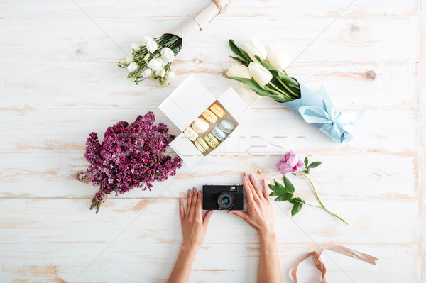 Stock photo: Hands of young woman holding photo camera on wooden table