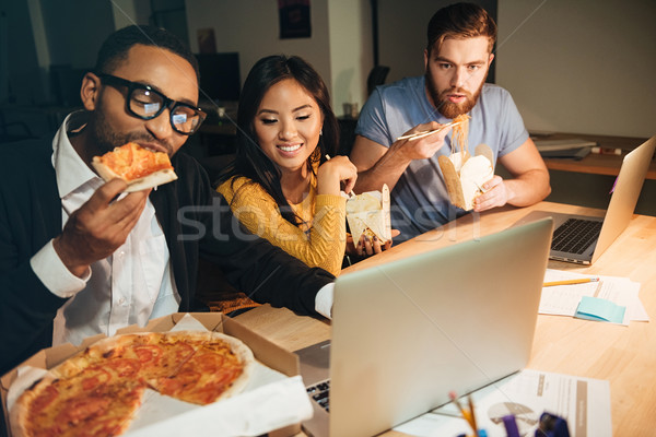 Happy colleagues working at night with laptops while eating pizz Stock photo © deandrobot