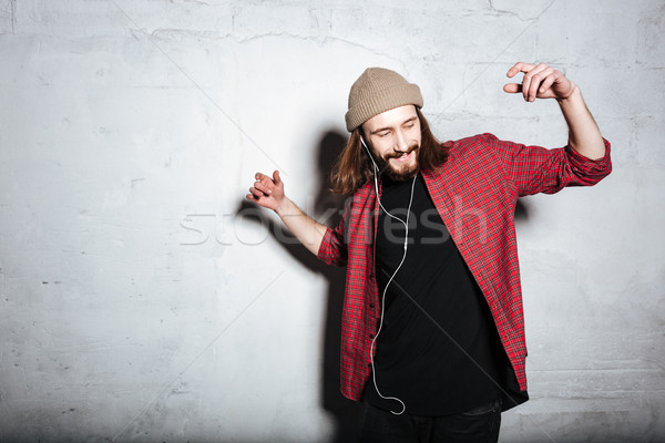 Stock photo: Happy young bearded hipster man listening music with earphones.