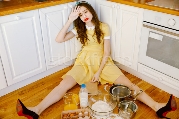 Sad tired young pin-up woman sitting on floor and cooking. Stock photo © deandrobot