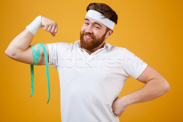 Portrait of smiling muscular man measuring bicep with measure tape Stock photo © deandrobot