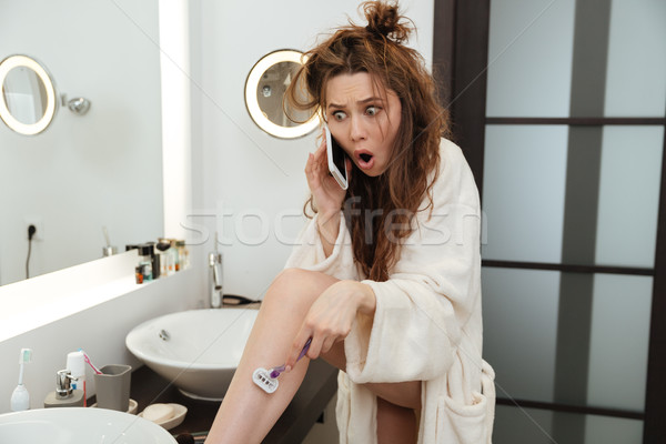 Astonished shocked woman shaving legs and talking on mobile phone Stock photo © deandrobot
