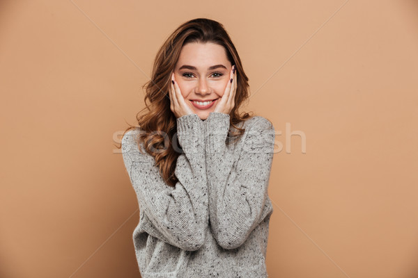 Cheerful brunette girl in gray jersey keeping hands at her face, Stock photo © deandrobot