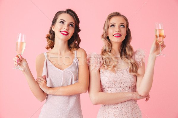 Two pleased women in dresses holding champagne and looking up Stock photo © deandrobot