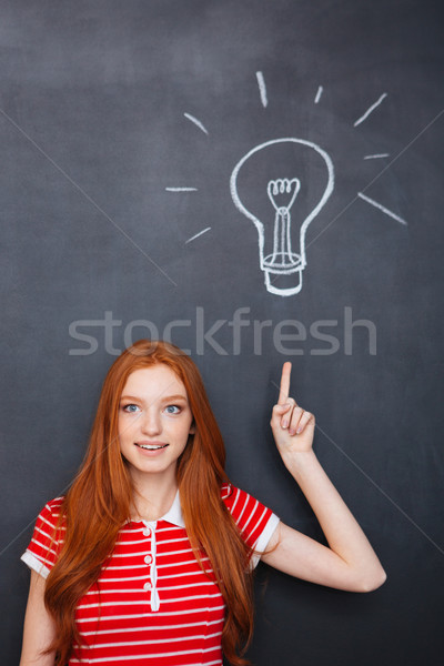 Attractive inspired woman pointing up and having idea over blackboard  Stock photo © deandrobot