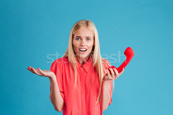 Puzzled worried blonde woman standing and talking on retro phone Stock photo © deandrobot