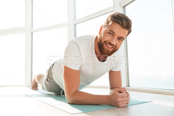 Smiling bearded man doing plank exercises over window background Stock photo © deandrobot
