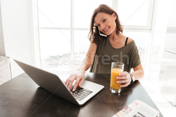 Smiling casual woman talking on smartphone, using laptop Stock photo © deandrobot