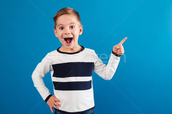 Happy young boy pointing up and holding arm on hip Stock photo © deandrobot