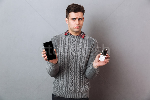 Confused man in sweater choosing between smartphones Stock photo © deandrobot