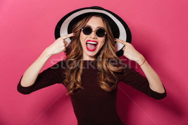 Happy lady wearing hat and sunglasses pointing. Stock photo © deandrobot