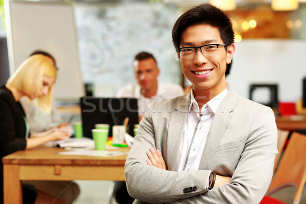 Portrait of cheerful businessman with arms folded sitting in front of colleagues Stock photo © deandrobot