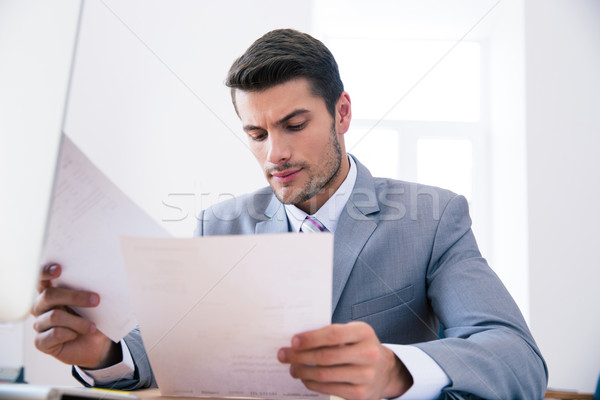 Confident businessman reading documents in office Stock photo © deandrobot