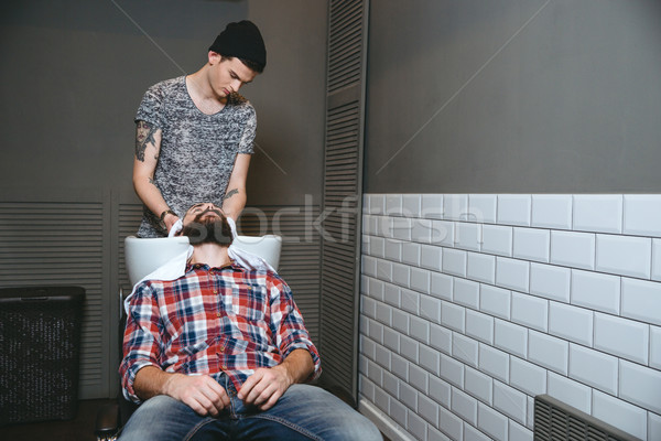 Young barber washing hair of client with beard in barbershop Stock photo © deandrobot