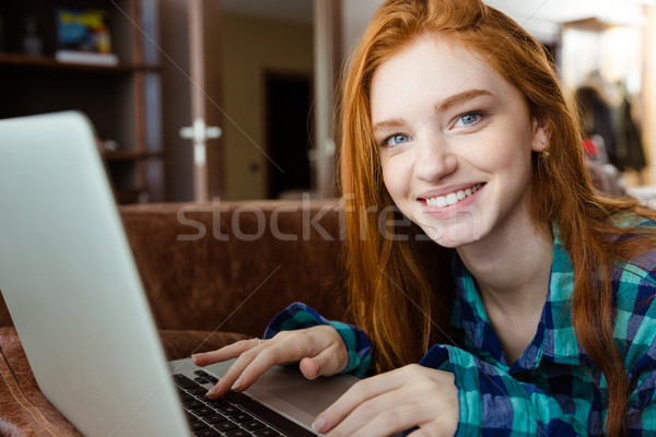 Smiling woman lying on brown sofa and using laptop Stock photo © deandrobot