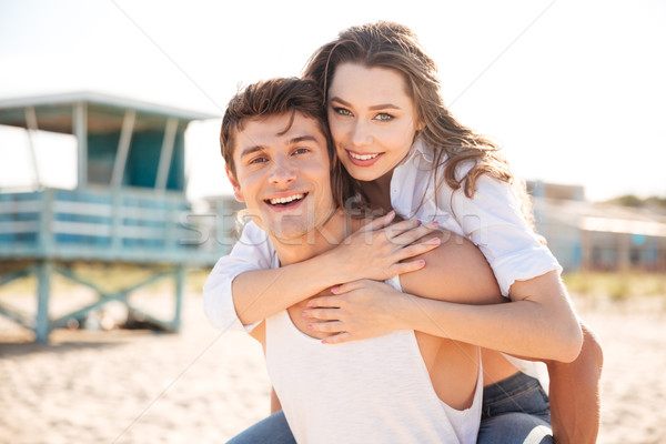 Cheerful young man piggybacking his girlfriend on the beach Stock photo © deandrobot
