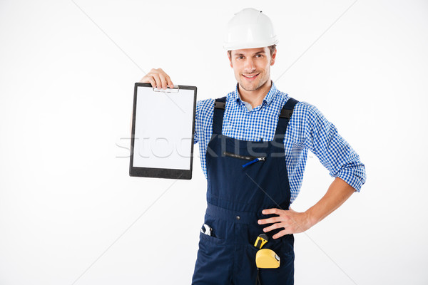 Stock photo: Smiling handsome builder showing blank sheet of paper on clipboard