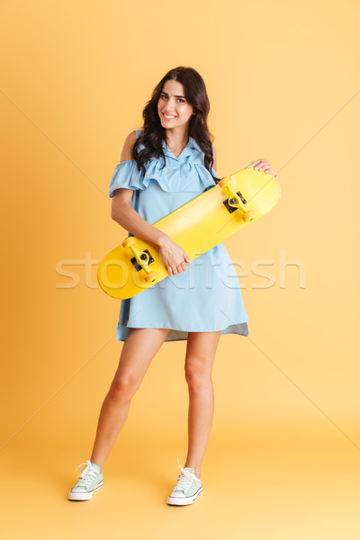 Smiling brunette woman in blue dress holding yellow skateboard Stock photo © deandrobot