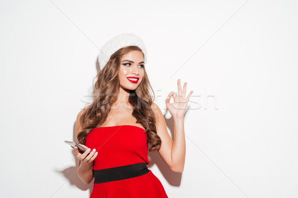 Smiling woman in red santa claus outfit holding mobile phone Stock photo © deandrobot