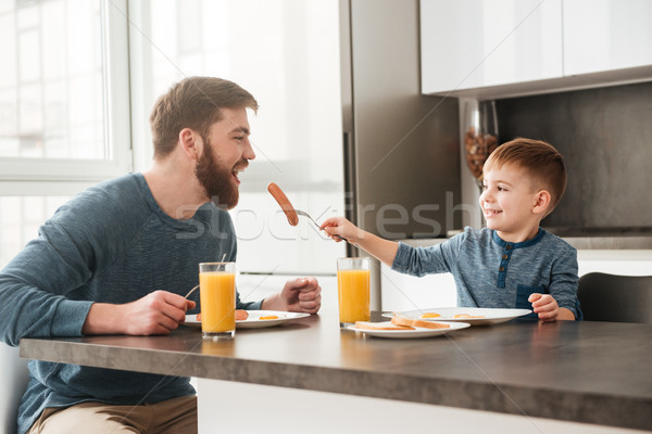 Cheerful bearded father eating at kitchen with his little son Stock photo © deandrobot