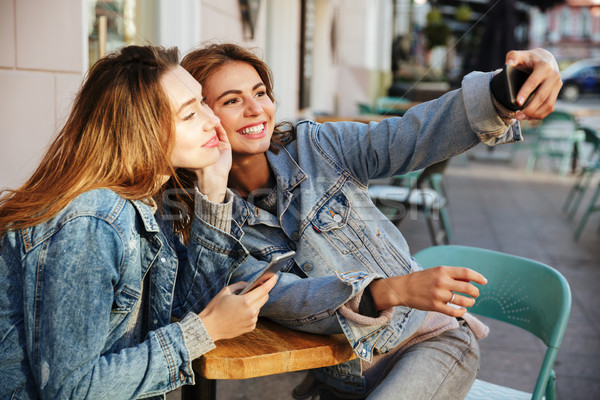 Photo of two charming brunette woman taking selfie on mobile pho Stock photo © deandrobot