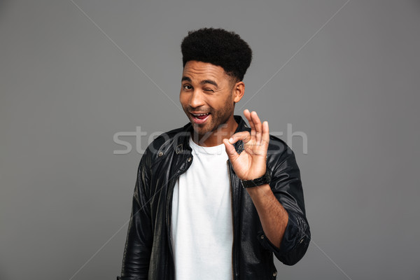 Young friendly african guy winks one eye while showing OK gestur Stock photo © deandrobot