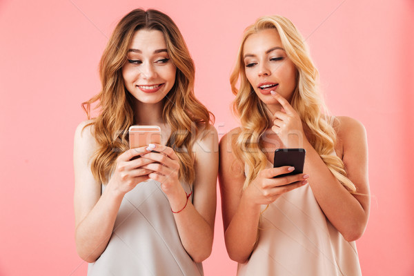 Two joyful women in pajamas looking to each other smartphones Stock photo © deandrobot