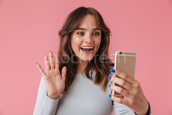 Portrait of a smiling young girl waving at mobile phone Stock photo © deandrobot