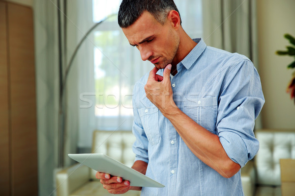 Handsome man standing and using tablet computer at home Stock photo © deandrobot