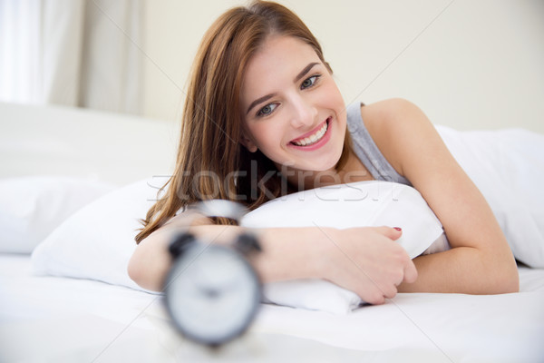 Pretty happy girl waking up in the morning and looking on alarm clock Stock photo © deandrobot