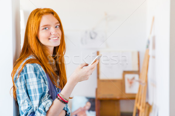 Charming happy young woman using smartphone in art workshop Stock photo © deandrobot