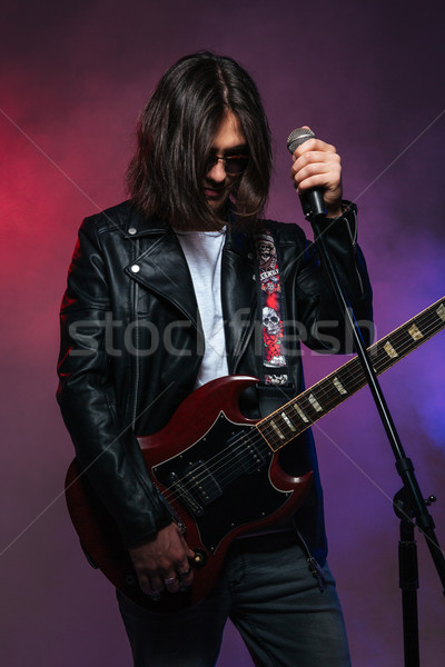 Serious young singer standing with microphone and electric guitar  Stock photo © deandrobot
