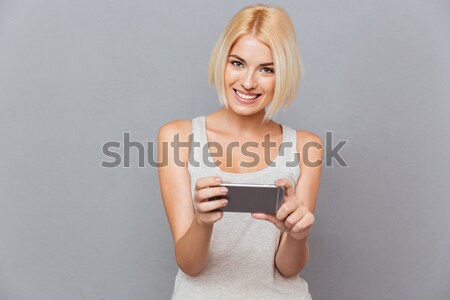 Portrait of happy charming young woman smiling and using smartphone Stock photo © deandrobot