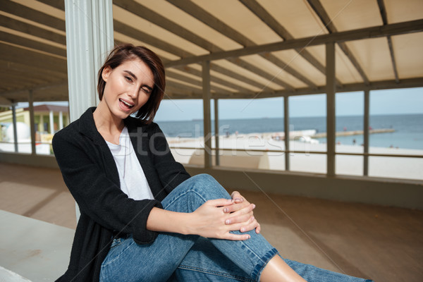 Cheerful woman sitting and winking in gazebo on the seaside Stock photo © deandrobot