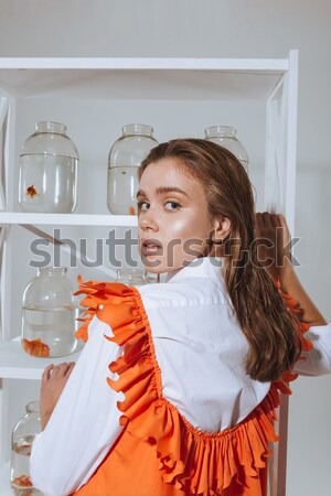 Woman putting jar with gold fish on the shelf Stock photo © deandrobot