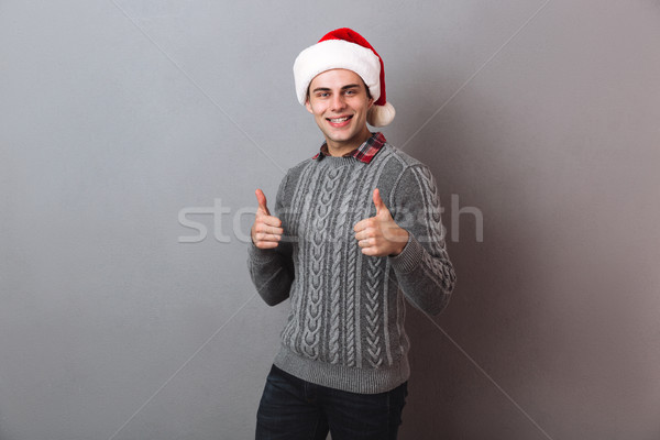 Smiling man in sweater and christmas hat showing thumbs up Stock photo © deandrobot
