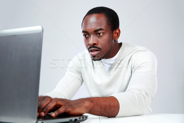 Concetrated african man using laptop on gray background Stock photo © deandrobot