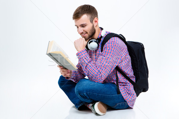 Cheerful handsome bearded man with backpack and headphones reading book  Stock photo © deandrobot
