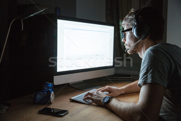 Focused man using earphones and computer in dark room  Stock photo © deandrobot