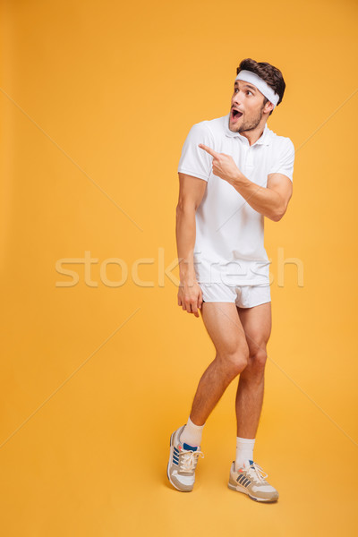 Surprised young man athlete with opened mouth pointing away Stock photo © deandrobot
